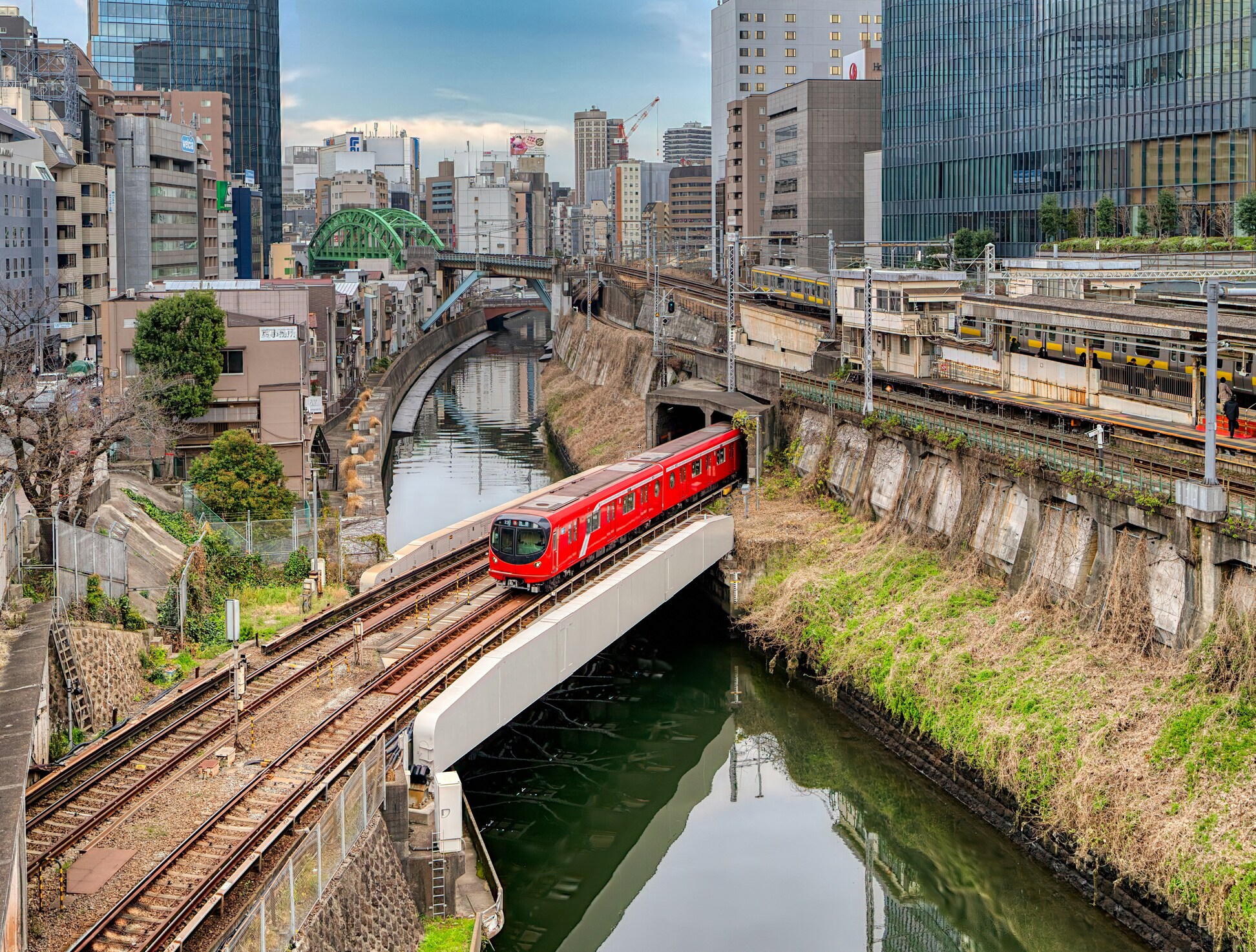 都市の高架橋を走る赤い電車と運河